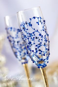 two wine glasses decorated with blue flowers and gold stemers on a table top,