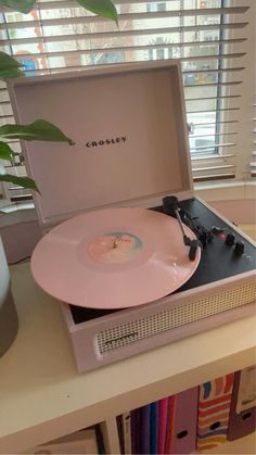 a pink record player sitting on top of a table next to a bookcase and window