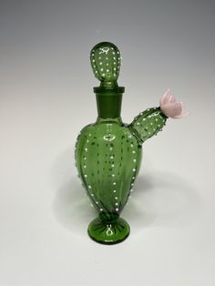 a green glass vase with a pink flower in the middle and white dots on it