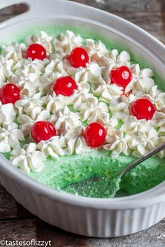 a green cake with cherries and whipped cream in a white dish on a wooden table