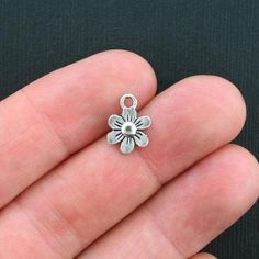 a hand holding a small silver flower charm