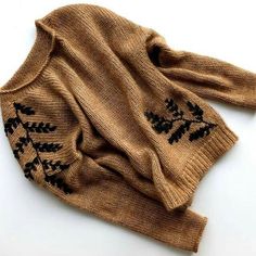 a brown sweater with black embroidered leaves on the front and back, sitting on a white surface