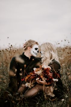 a man and woman sitting in tall grass with a skeleton mask on their face