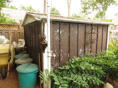 an outhouse with trash cans next to it and plants in the foreground, on a sunny day