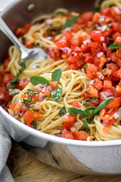 a bowl filled with pasta and vegetables on top of a wooden table next to a fork