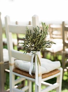 an olive branch tied to the back of a wooden chair with white linens on it