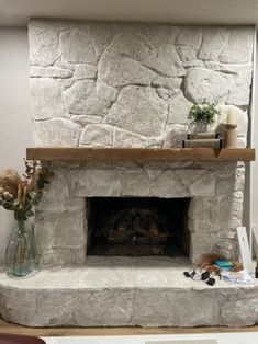 a stone fireplace in a living room next to a chair and vase with flowers on it