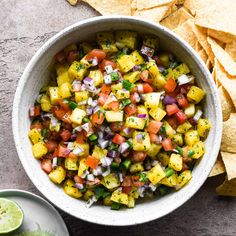 a white bowl filled with pineapple salsa next to tortilla chips and lime wedges