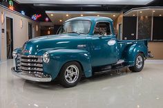 an old blue truck is parked in a showroom with neon signs on the walls