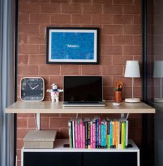 a laptop computer sitting on top of a wooden desk next to a clock and bookshelf