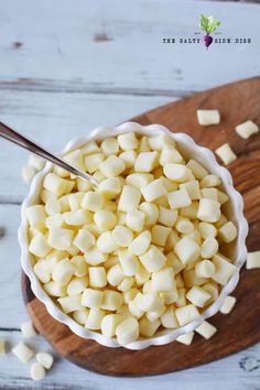 a wooden cutting board topped with a white bowl filled with diced potatoes