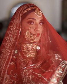 a woman wearing a red bridal veil with gold jewelry on her face and nose