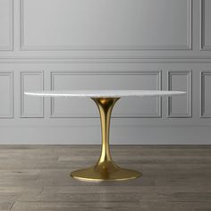 a white marble table with gold pedestals in front of a gray wall and wooden floor