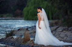 a woman in a wedding dress standing on rocks by the water at sunset with her back to the camera