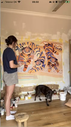 a woman is painting a tiger on the wall with a dog in front of her