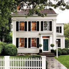 a white house with black shutters on the front and green door, surrounded by trees