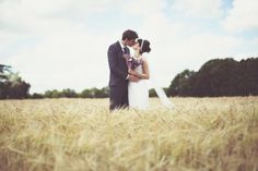 a bride and groom kissing in the middle of a wheat field with trees in the background