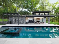 an outdoor kitchen next to a swimming pool in the middle of a yard with trees and grass