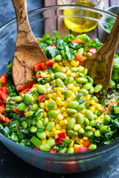 a glass bowl filled with vegetables and two wooden spoons on top of the bowl