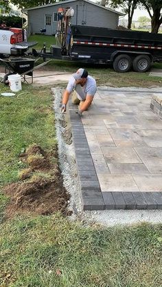 a man laying bricks on the ground in front of a house with a truck behind him