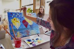 two girls are painting on canvases in an art studio