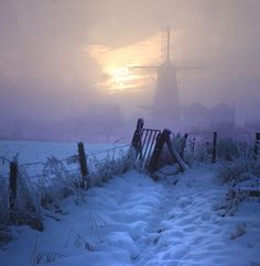 the sun is setting behind a windmill on a snowy day