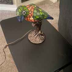 a stained glass bird lamp sitting on top of a black table in a living room