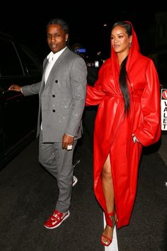 a man in a suit and woman in a red coat are walking down the street