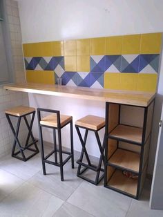 three stools and a counter in a room with tiled walls behind them, along with shelves on the wall