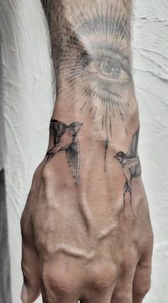 a man's hand with an all seeing eye tattoo on his left wrist and two birds flying around it