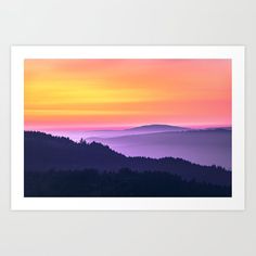 a colorful sunset over the mountains with trees in the foreground and clouds in the background