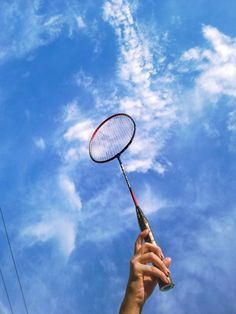 a person holding a tennis racket up in the air against a cloudy blue sky