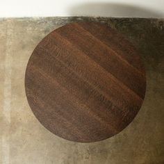 a round wooden table sitting on top of a cement floor next to a white wall