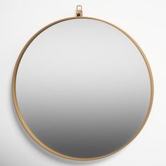 a round mirror hanging on the wall next to a white wall with a gold frame