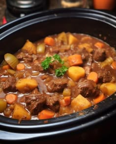 a crock pot filled with beef stew and carrots on top of a table