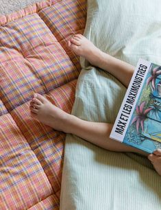 a person laying on a bed with a book in their hand and feet propped up against the pillow