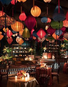 many lit up lanterns hang from the ceiling above tables with chairs and tablecloths on them