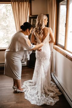 two women in white dresses standing next to each other near a window and looking out the window