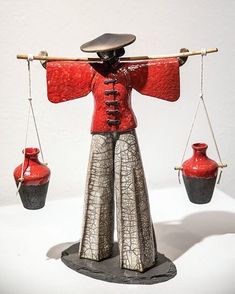 a figurine holding two red vases on one end and another hanging from the other