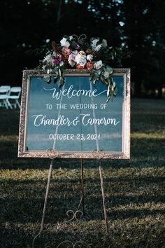 a welcome sign with flowers and greenery on it in front of a grassy field