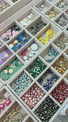 many different colored and shaped buttons are in a white box with trays full of them