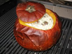 a large red pumpkin sitting on top of a bbq grill covered in rice and meat