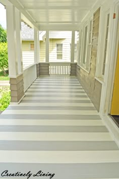 an empty porch with white and gray stripes on the floor next to a yellow door