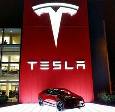 a red tesla car is parked in front of a building with the word tesla on it