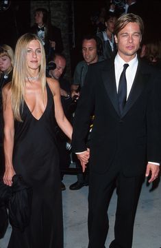 a man and woman in formal wear holding hands while walking down the red carpet at an event