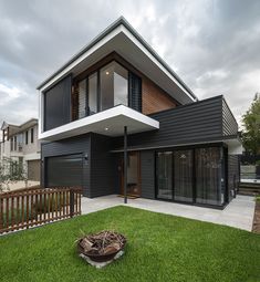 a modern house with black sidings and white trim on the roof, grass in front of it