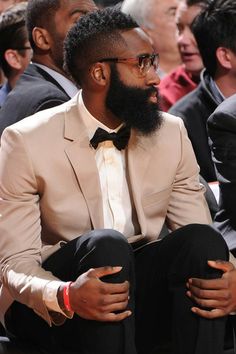 a man with a beard and glasses sitting in front of other men at a basketball game