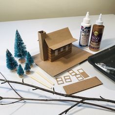 some crafting supplies are sitting on a table next to small trees and glue bottles