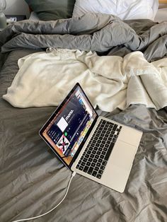 an open laptop computer sitting on top of a bed next to a white pillow and blanket