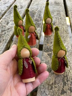 a hand is holding several small green gnomes on a wooden bench, with one wearing a red dress